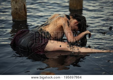 Young woman bathing in therapeutic water of mud estuary, next there are wooden columns. Spa.