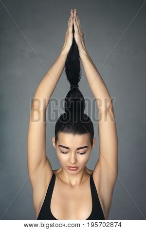 Brunette fashion attractive girl holding and pull a ponytail. Profile of beautiful mixed race Asian Caucasian female model posing with simple hairstyle against gray background.