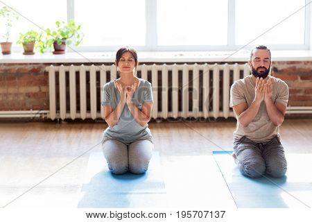 fitness, people and healthy lifestyle concept - man and woman doing lotus seal gesture and meditating in seated pose at yoga studio