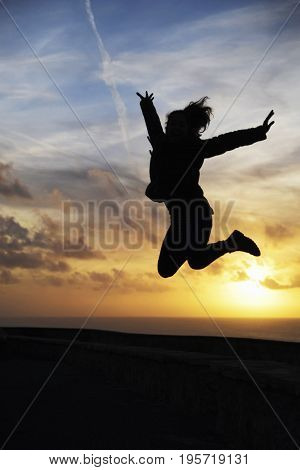 Happy girl jumping with a beautiful sunset as background