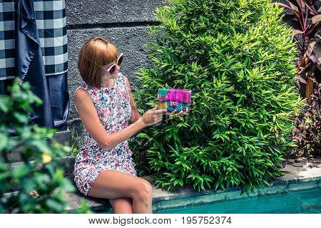 Summer portrait of a beautiful sexy girl with sunglasses and luxury handmade snakeskin python handbag in the swimming pool. Fashion outdoor. Tropical Bali island.
