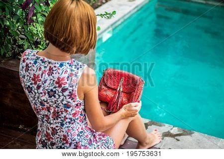 Summer portrait of a beautiful sexy girl with sunglasses and luxury handmade snakeskin python handbag in the swimming pool. Fashion outdoor. Tropical Bali island.