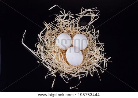 Three chicken eggs in the nest like On a black background