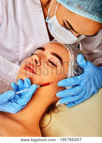 Filler injection for female face. Removing wrinkles. Beauty woman giving injections in cosmetology room. Doctor in medical mask and gloves with syringe injects cheeks drug