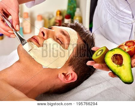 Facial mask from fresh fruits and clay for man. Beautician apply slices of avocado, grapefruit and kiwi. Mask made of healing clay, close-up. Avocados main ingredient cosmetic masks.