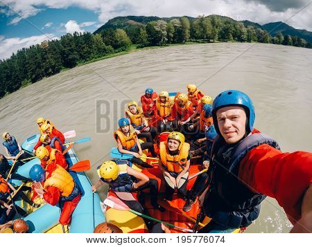 mountain Altai, RUSSIA - July 16, 2017: man in a helmet holds an action camera and makes selfie on the background of friends with oars, rafting