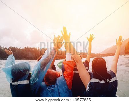 Friends of the team are riding in an inflatable boat with a motor and raised their hands up - happy, rafting.