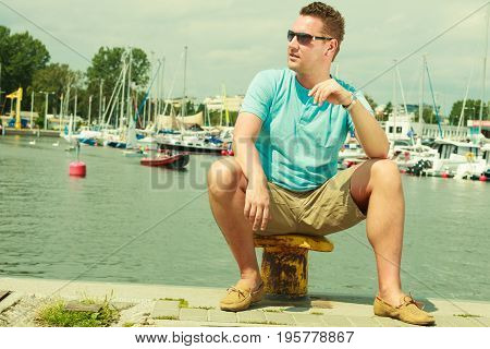 Summertime vacation adventure concept. Man spending his free time walking on marina sightseeing during summer guy sitting on bitt.