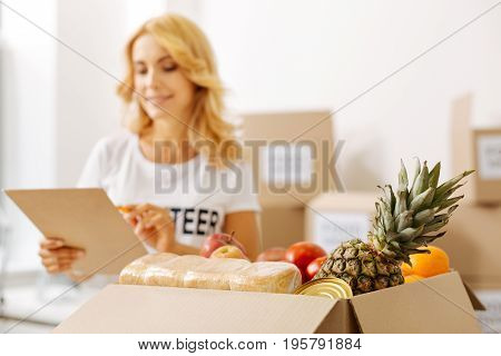 Double check. Energetic attentive intelligent lady looking at her list and checking the contents of the boxes making sure the foods packed right