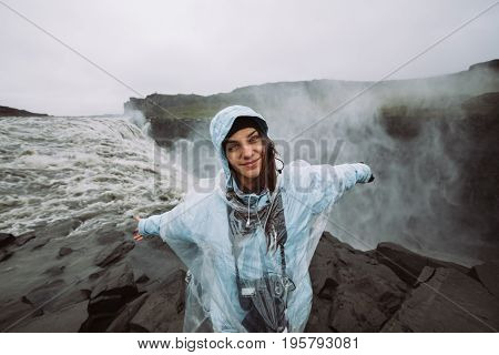 Young joyful hiker female smiling near Dettifoss waterfall in Vatnajökull National Park in Northeast Iceland.Tourist visiting Iceland and touring through ring road.Exploring.Nature photographer.