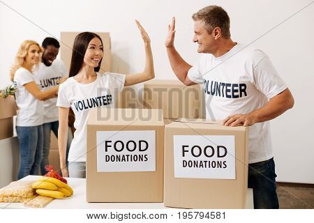 Making the world a better place. Vibrant emotional energetic men and women looking excited while giving his colleague a high five as they working pro bono in charitable organization