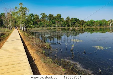 Mysterious wooden path towards Neak Pean Temple through artificial island in Angkor Complex, Siem Reap, Cambodia. Ancient Khmer architecture, famous Cambodian landmark, World Heritage