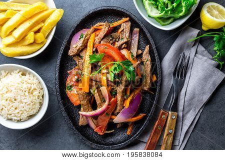 Peruvian dish Lomo saltado - beef tenderloin with purple onion, yellow chili, tomatoes served on black plate with french fries and rice. Top view