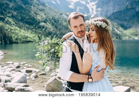 bride with the beautiful blue dress and groom hugging with views of the beautiful green mountains and lake with blue water