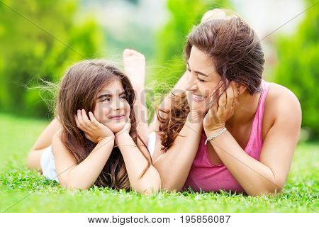 Portrait of a mother with little pretty daughter having fun together outdoors, lying down on the meadow and looking on each other, spending summer holidays in a countryside, happy family life