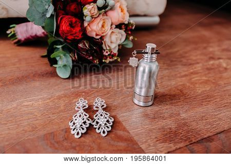 Beautiful bridal earrings and perfume on the wooden floor next to the wedding bouquet. Selective focus
