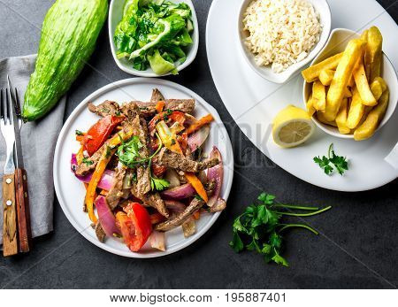 Peruvian dish Lomo saltado - beef tenderloin with purple onion, yellow chili, tomatoes served on white plate with french fries and rice. Top view