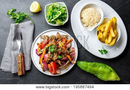 Peruvian dish Lomo saltado - beef tenderloin with purple onion, yellow chili, tomatoes served on white plate with french fries and rice. Top view