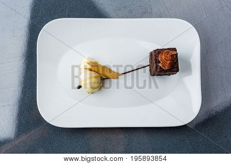 One scoop of the ice cream served on the white plate with brownie and buscuit