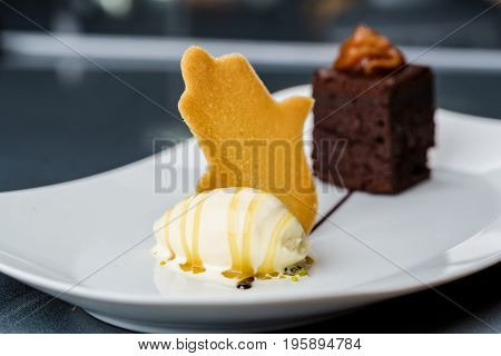One scoop of the ice cream served on the white plate with brownie and buscuit
