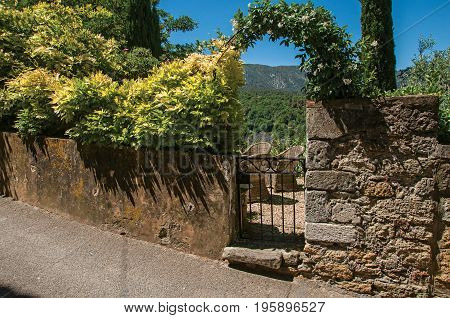 View of small garden behind iron gate and stone wall in the village of Ménerbes. Located in the Vaucluse department, Provence-Alpes-Côte d'Azur region, southeastern France