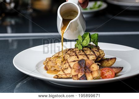 Grilled chicken fillet served with french fries, asparagus and cherry tomatoes, decorated with grilled garlic and baby spinach