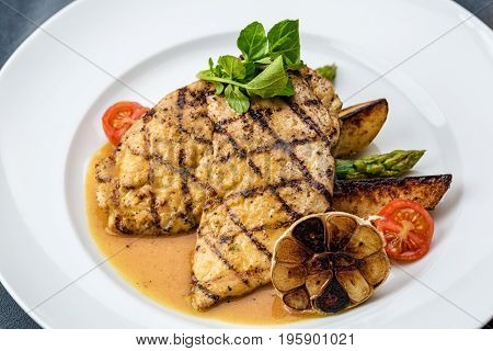 Grilled chicken fillet served with french fries, asparagus and cherry tomatoes, decorated with grilled garlic and baby spinach