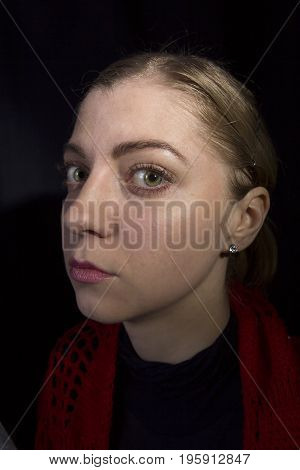 Strange young blonde woman close-up on a black background