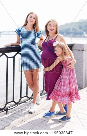 Samesex lesbian family with child on a walk in the park near the river. Lesbians mothers with adopted child, happy family, pregnant couple with kid