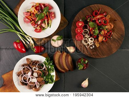 Three dishes stand on dark stone background. Fresh low-calories salad healthy snack main course. Ingredients mushroom tomato onion carrot garlic pepper chicken breast greens spices. Top view