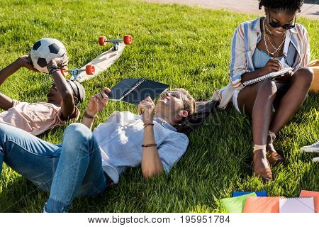 mutiethnic students lying on green grass while studying in park