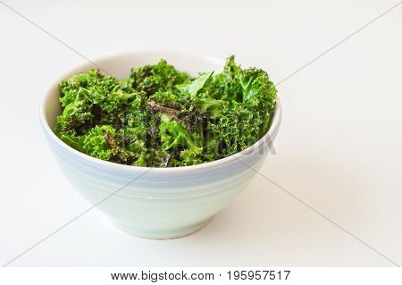 Kale chips and fresh kale leaves with oil in blue bowl on white background. Kale salad
