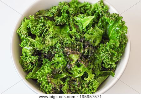 Kale salad in big bowl on white table. Fresh oily kale leaves. Healthy food