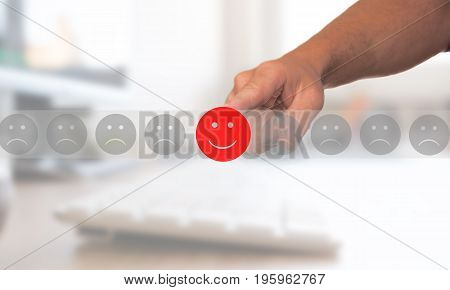 Man hand selects a happy red emoticon among other sad gray face
