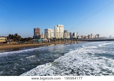 DURBAN SOUTH AFRICA - JULY 7 2017: Early morning view of waves breaking on beach against blue Durban city skyline in South Africa