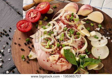 Cooking fresh chicken fillet with fresh vegetables and spices seasoning on rustic wooden board. The table with the ingredients for the dishes. Dark stone background. Healthy low-calories food.