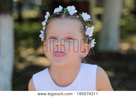 Little girl shows tongue child with wreath of artificial flowers on head