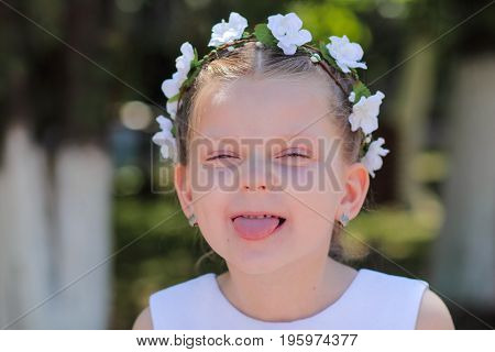 Little girl shows tongue child with wreath of artificial flowers on head