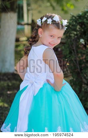 cute smiling girl dressed in blue and white dress with a wreath of artificial flowers on her head child in a festive dress on a nature background half-turn