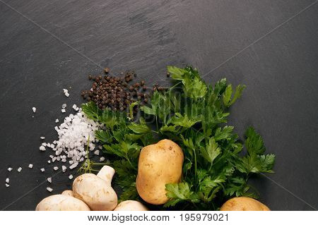 Raw fresh onions potatoes garlic mushroom greens and seasoning on dark stone background with copy space. Top view ingredients for cooking a delicious cream soup. Healthy vegetarian food.