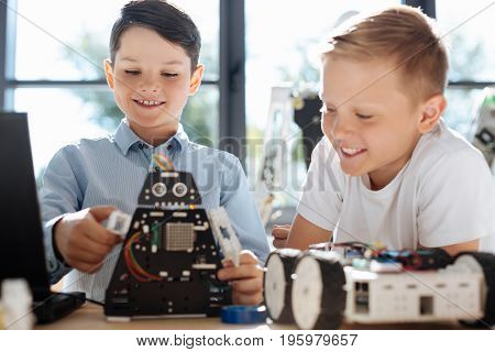Cool toy. Pleasant pre-teen boy showing the work of his black robotic cosmic warrior to his friend looking at it with smile