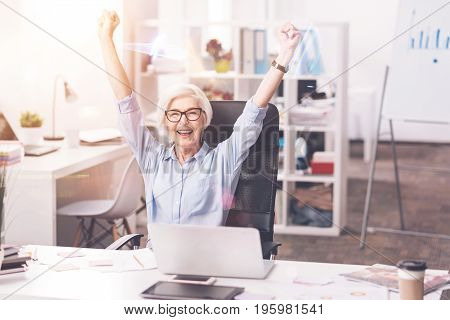 I did it. Accomplished professional business lady enjoying her success by putting her hands up after completing a project