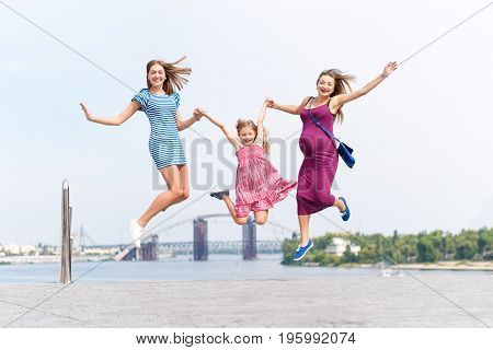 Samesex lesbian family with child on a walk in the park near the river. Lesbians mothers with adopted child, happy family, pregnant couple with kid