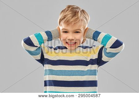noise, stress and people concept - stressed little boy in striped pullover closing ears by hands over grey background