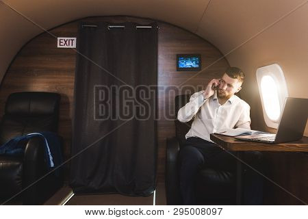 Young Attractive And Successful Businessman Talking On The Phone And Working While Sitting In The Ch