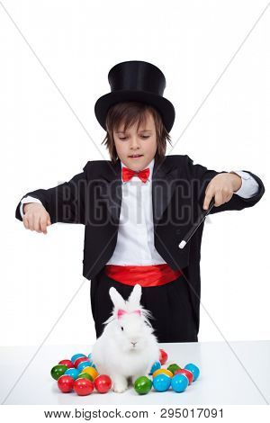 Magician boy perform a magic trick with the easter bunny and some colorful eggs - isolated on white