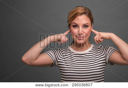 Attractive Woman Covers Her Ears With Her Fingers On A Gray Background.