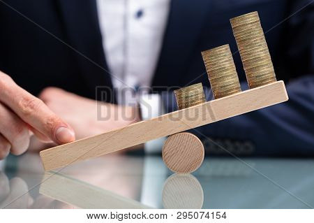 Close-up Of A Businessperson Balancing Increasing Stacked Coins With Finger On Seesaw