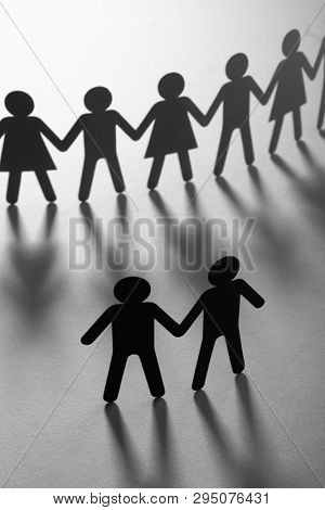Black paper figure of male couple in front of a crowd of paper people holding hands on white surface. Social movement, protest, minorities concept.