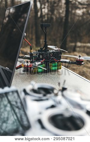 Fpv Drone Lies On The Table Near The Laptop And Control Panel. The Pilot Sets Up His Racing Drone Be